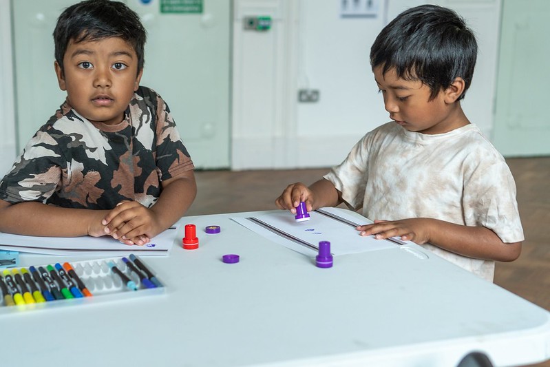 Two young boys sit at a table doing a colouring activity