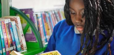 A girl dressed in a blue school sweatshirt concentrates as she reads a book