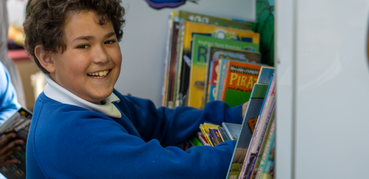 A boy smiles at the camera while browsing for books in a children's library