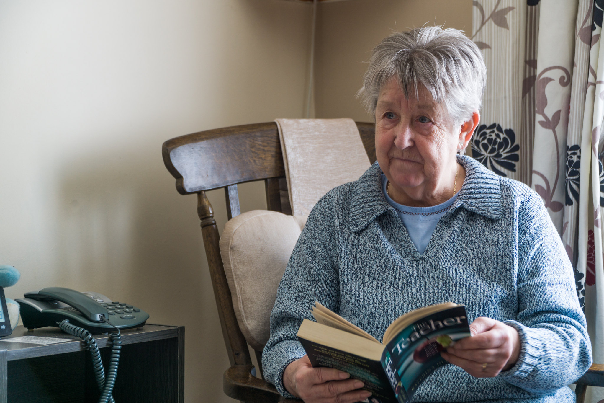 A woman sits in a chair reading a book to someone out of shot