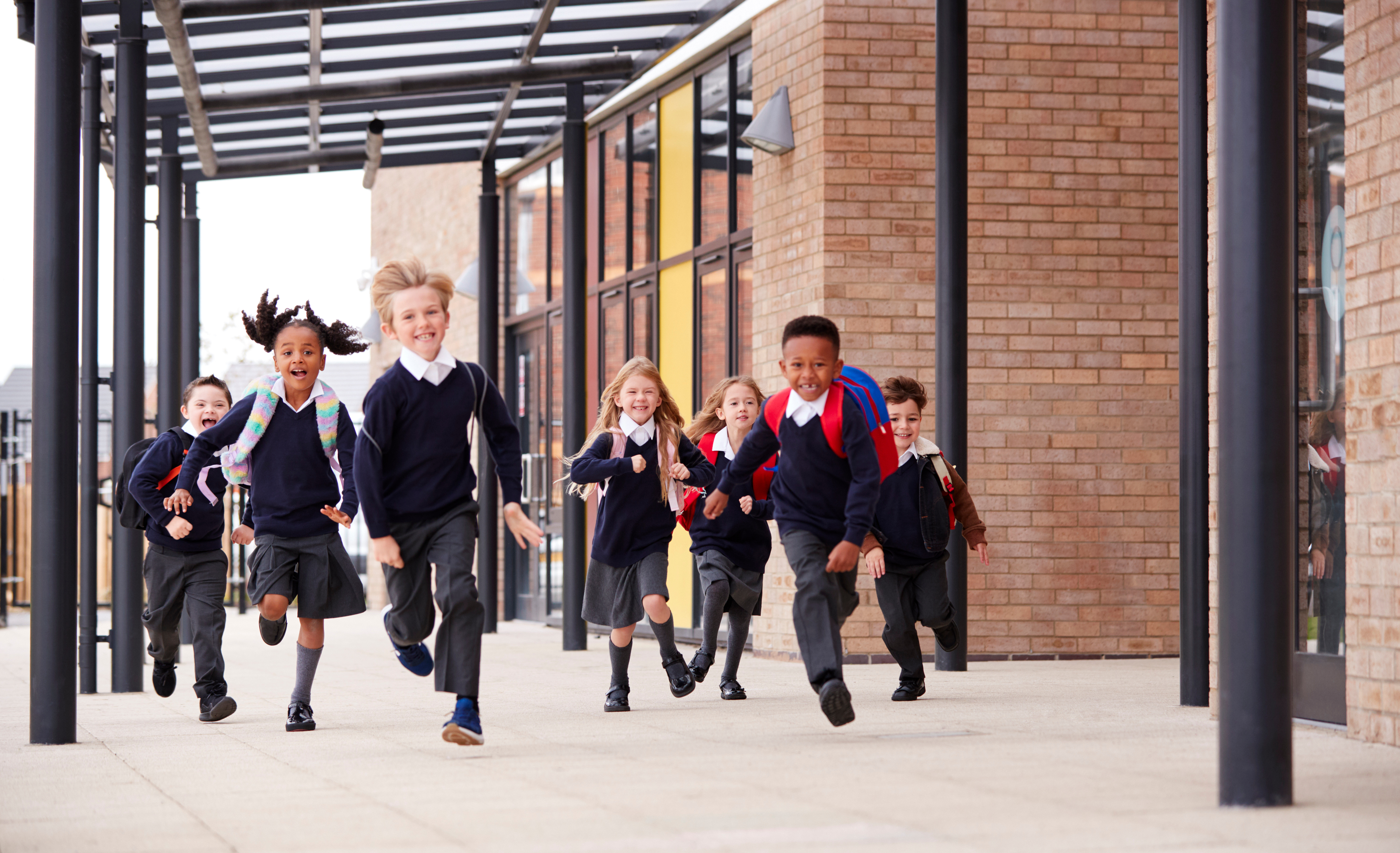 Seven primary school children run smiling towards the camera.