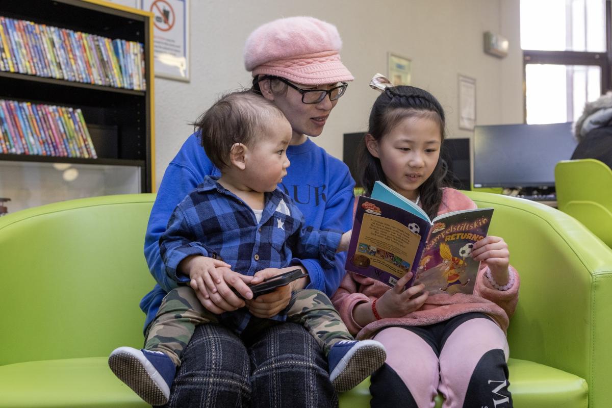 Woman reading with two children in a library Woman reading with two children in a library