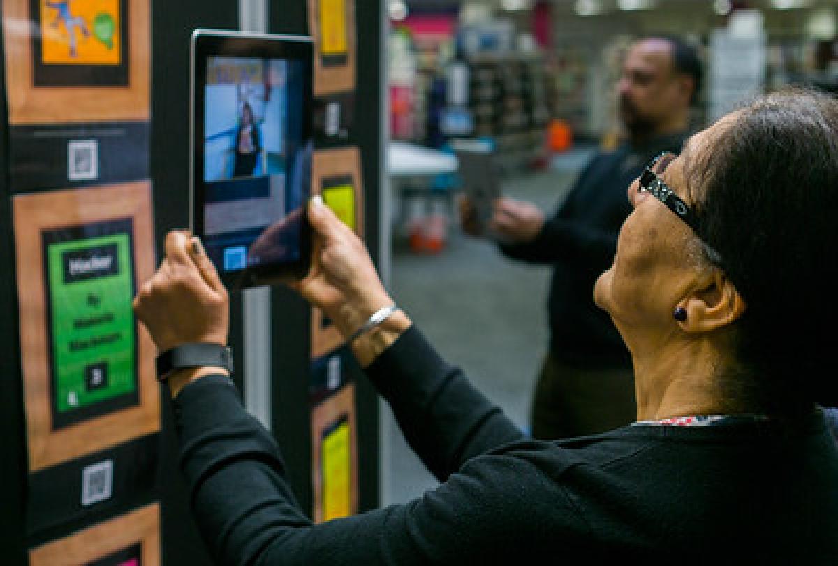 A woman holds up a tablet in front of her face in a library A woman holds up a tablet in front of her face in a library