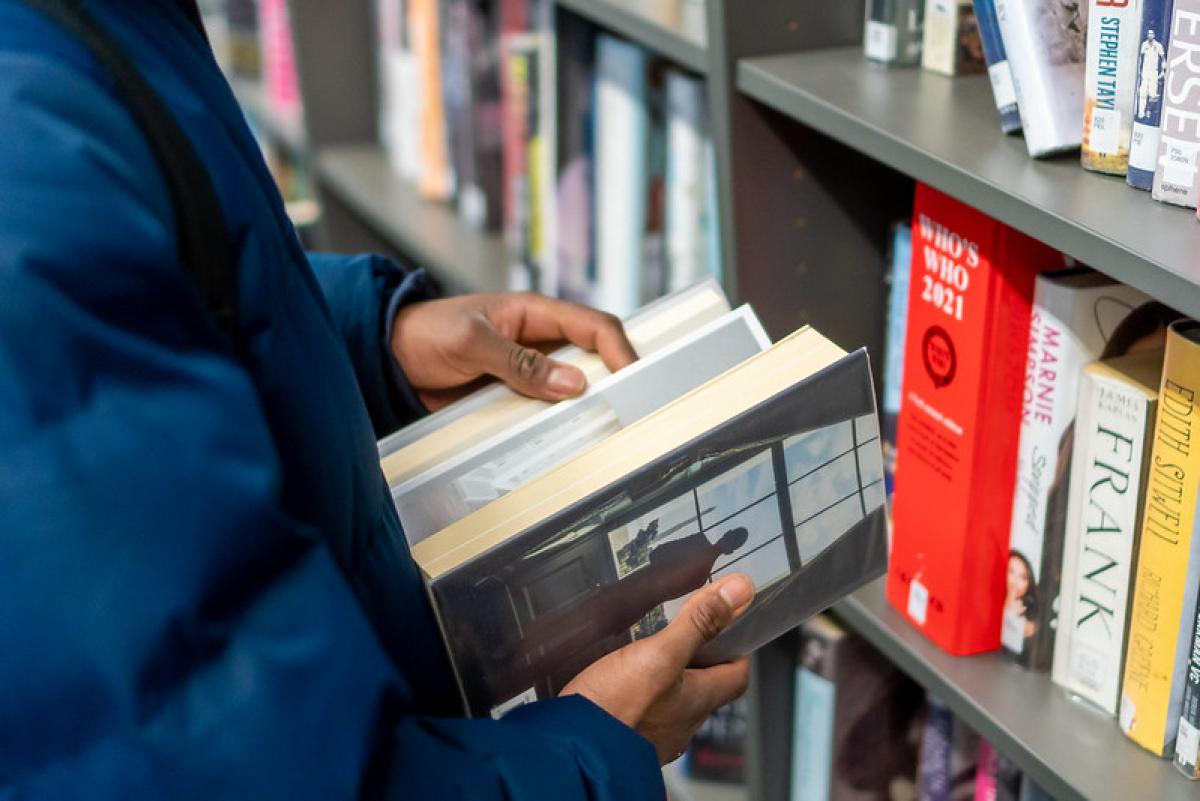 A hand leafs through an open book inside a library A hand leafs through an open book inside a library