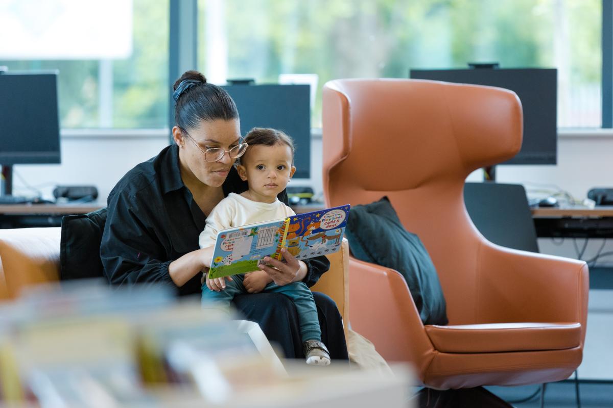 A mother reads to a young child in a library.