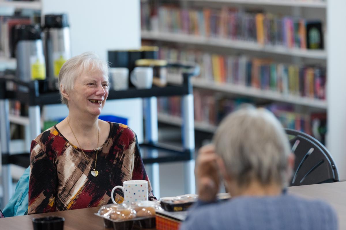 A woman smiles as she talks in a library.