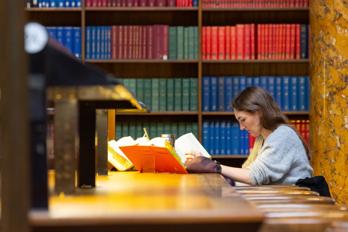 A woman sits at a desk in a library reading.