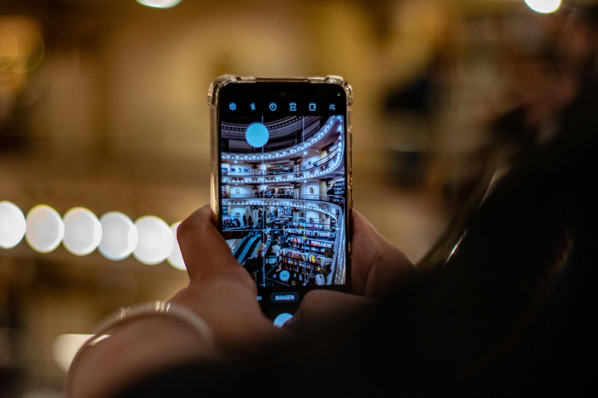 A person holding a smartphone and photographing the interior of a public library, which is visible on the phone screen.