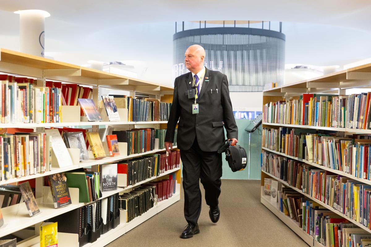 An older man walks between library shelves.