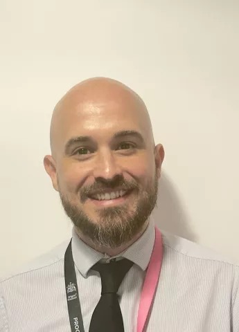 Craig Jones smiles into the camera. He is wearing a black tie.