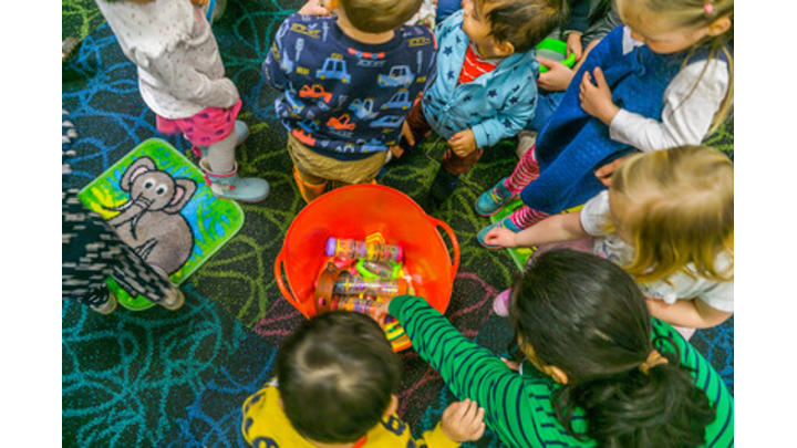 A circle of children play with toys in an orange bucket