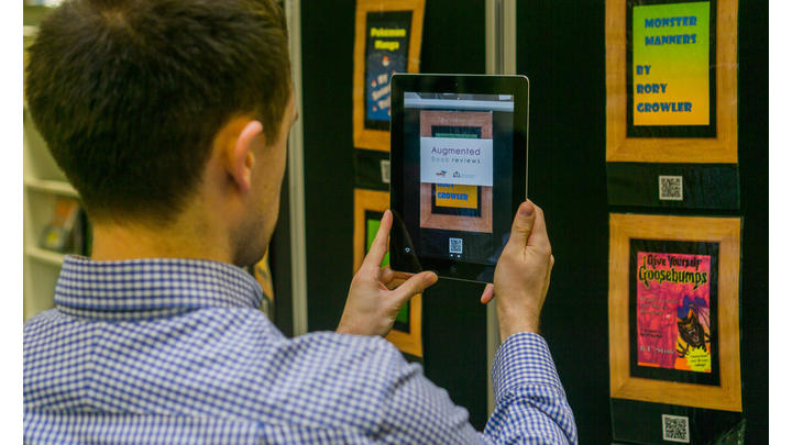 Young man holding up a tablet to view an augmented book