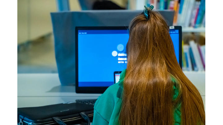 The back of a young girl's head as she works at a computer screen in a library