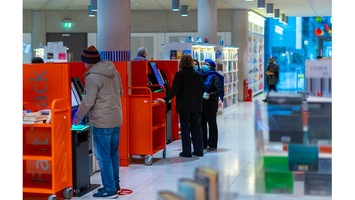 A group of people use red return shelves in a library.