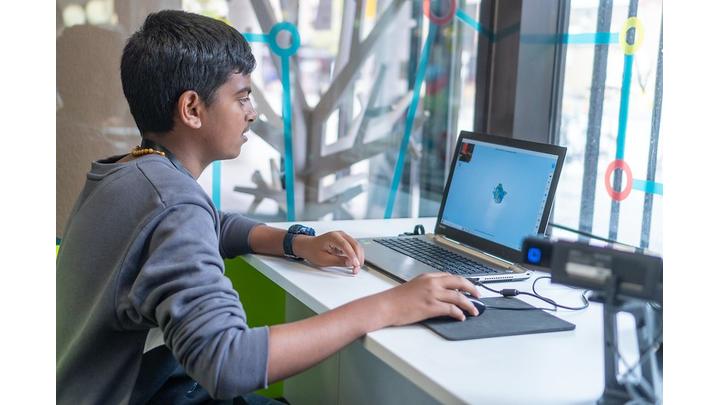A boy sits working at a laptop in a library.