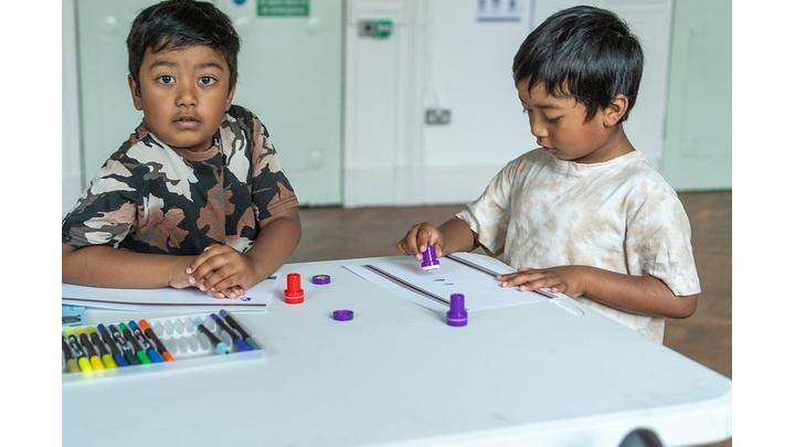 Two young boys sit at a table doing a colouring activity