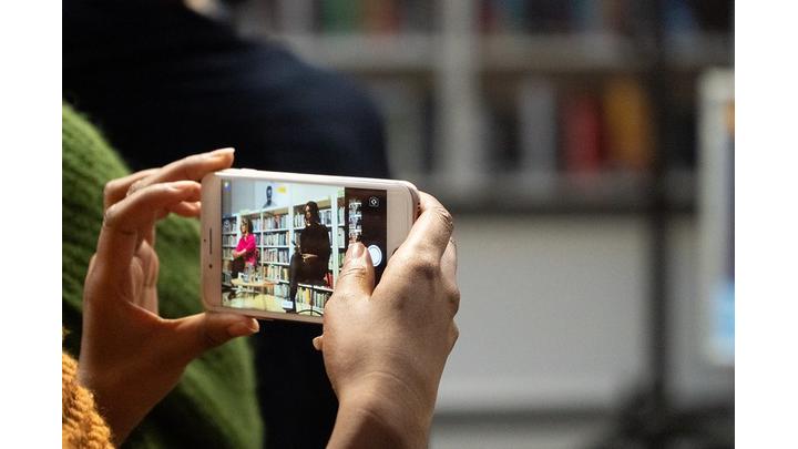 A smartphone captures an event in a library. The event is in progress and is being shown on the smartphone screen.