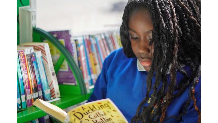 A girl dressed in a blue school sweatshirt concentrates as she reads a book