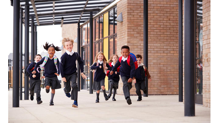 Seven primary school children run smiling towards the camera.
