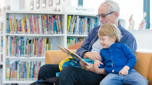 An older man reads to a young boy in a library.