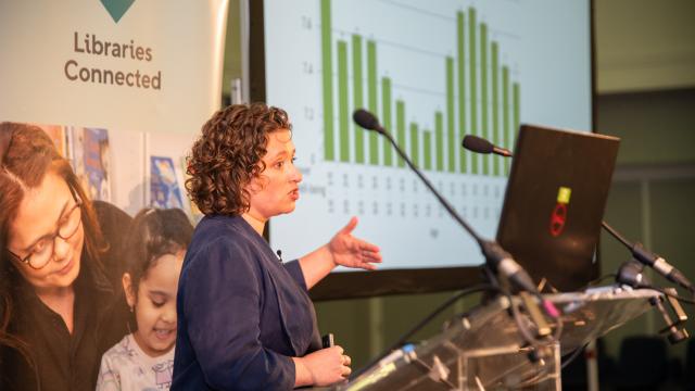 Photo of a female speaker with a graph in the background