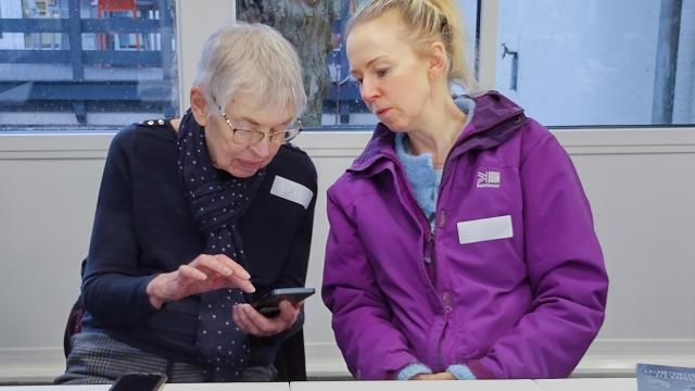 Volunteer supports an older adult to use a smartphone during a digital skills session.