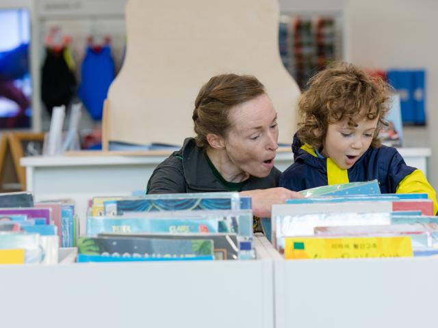 A woman smiles as she shows a child books in a library.