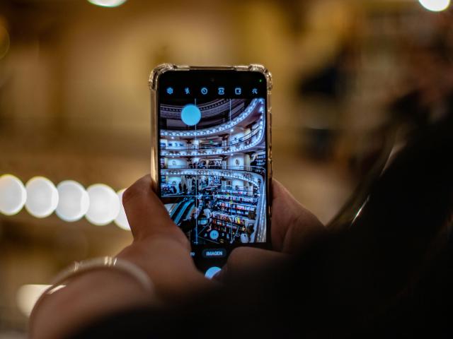 A person holding a smartphone and photographing the interior of a public library, which is visible on the phone screen.