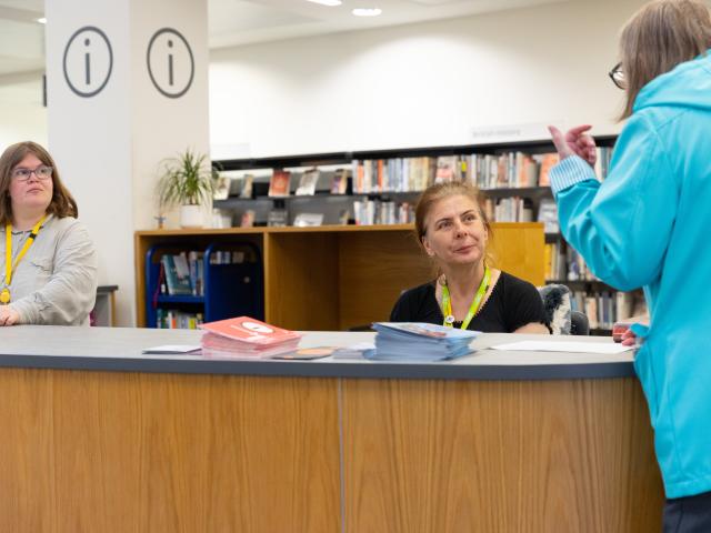 A female customer asks for advice at a library information desk.