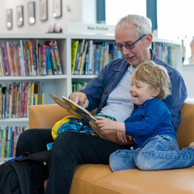 An older man reads a book to a smiling child.