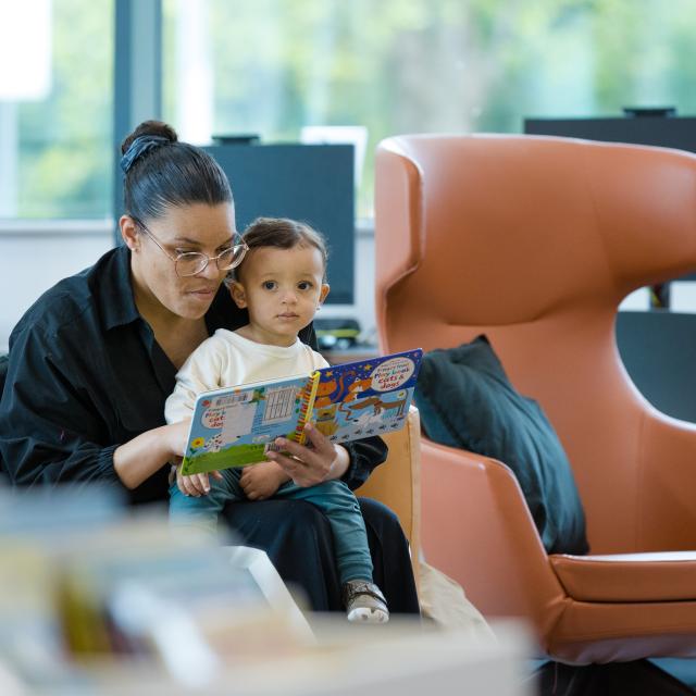 A mother reads to a young child in a library.