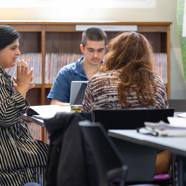 A woman speaks to a red haired woman in a library.