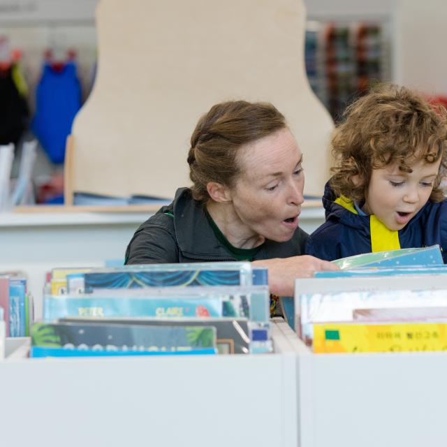 A woman smiles as she shows a child books in a library.