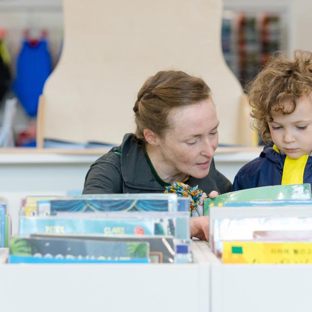 A female librarian reads with a child in a library.