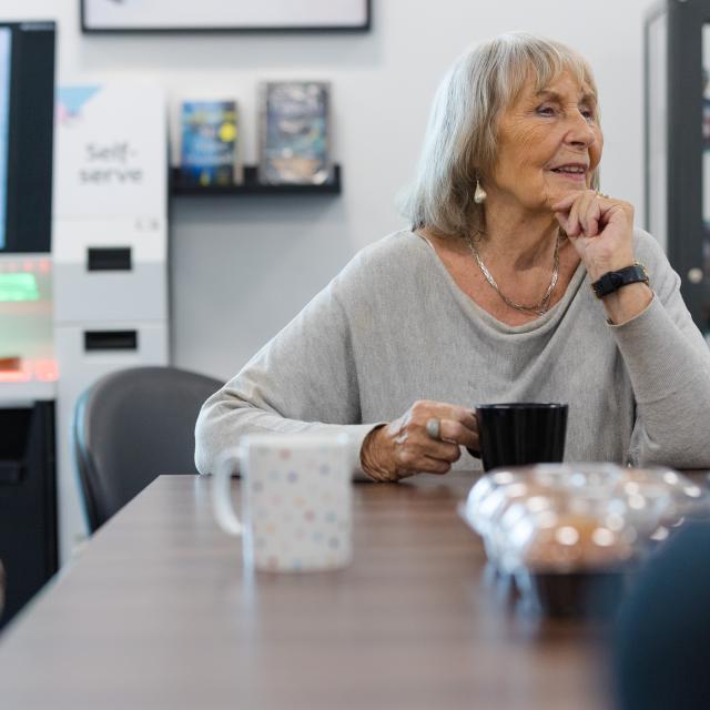 A woman rests her head on her hand as she sits with a black cup at a table.