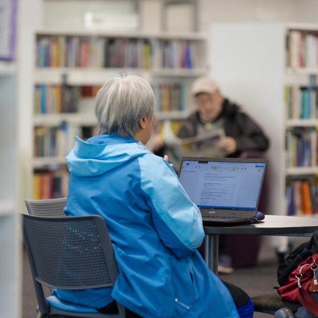 A woman sits in a library wearing a blue coat.