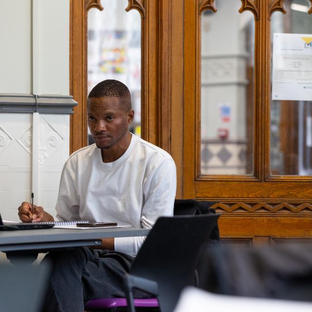 A young man works at a laptop in a library.