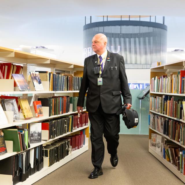 An older man walks between library shelves.