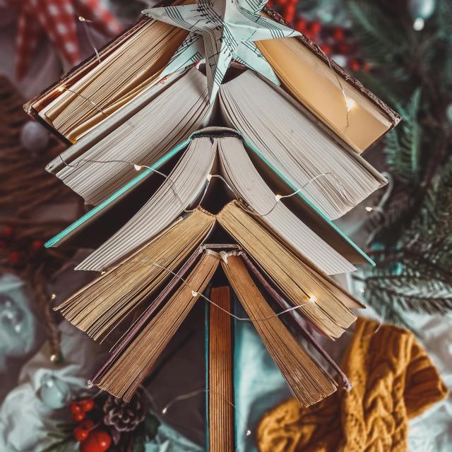 A Christmas tree made from stacked open books arranged in a triangular shape, topped with a star crafted from sheet music.
