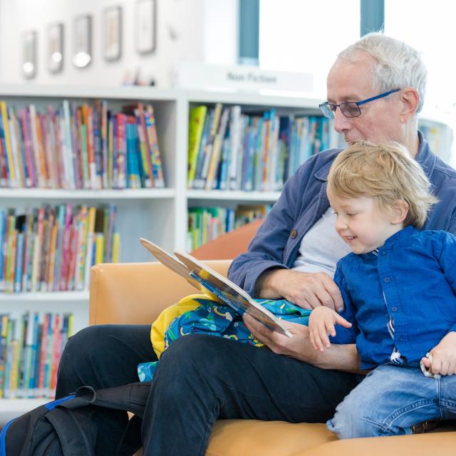 An older man reads to a young boy in a library.