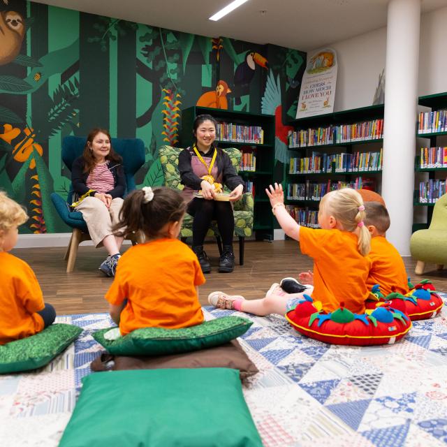Children dressed in orange listen to a storytime in a library.