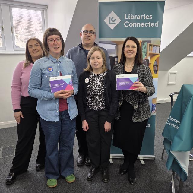 Emma Hoddinott is seen with others holding up a new guide helping library workers support communities with digital literacy.