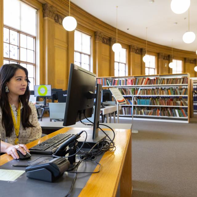 A female librarian sits working at a computer at an information desk.