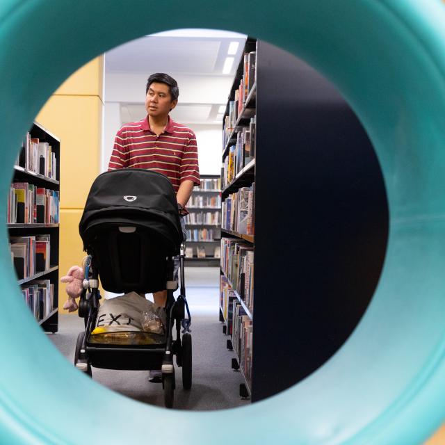 A man pushes a pushchair in a library.