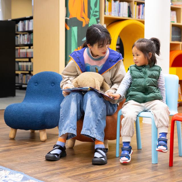 A woman reads a picture book to a child in a library.