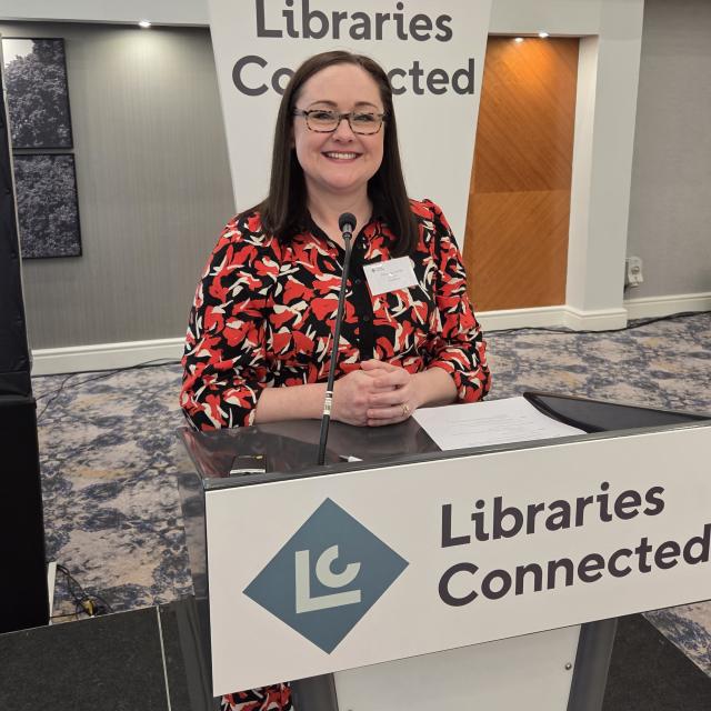 Librarian Amanda Jones stands behind a lectern displaying the Libraries Connected name and branding.