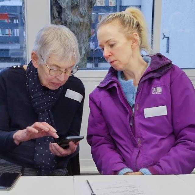 Volunteer supports an older adult to use a smartphone during a digital skills session.