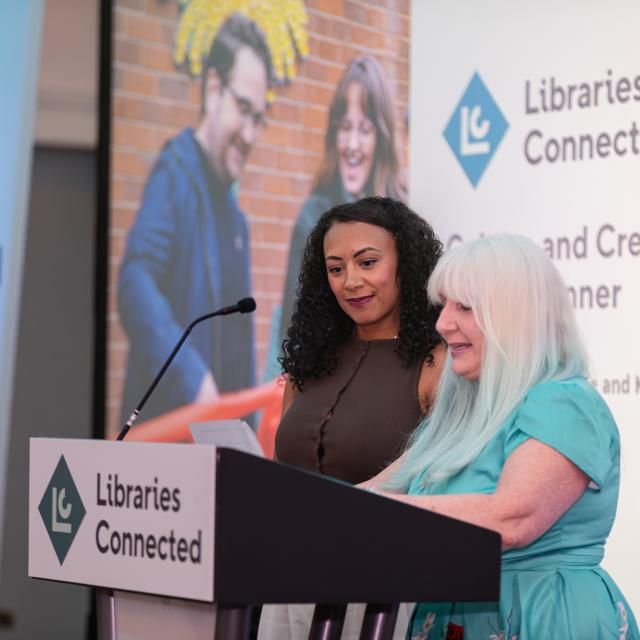 Two female award winners speaking at a lectern