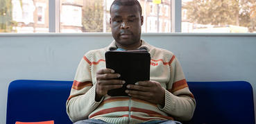 A man in a cream jumper reads from a tablet device.