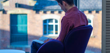 A seated man reads a book in a library